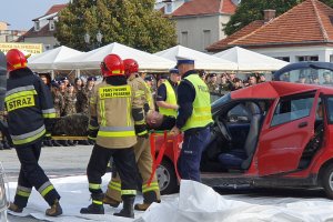 Strażacy przenoszą uczestnika wypadku drogowego wyciągniętego z pojazdu, podczas pokazów współdziałania służb na chełmińskim rynku