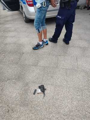 policjant i zatrzymany mężczyzna stoją przy radiowozie, na ziemi leżą przedmioty zawinięte w woreczek foliowy