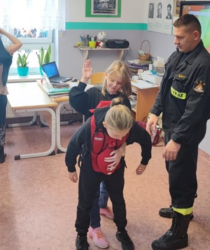 dzieci pod okiem strażaka ćwiczą udzielanie pomocy w sytuacji zakrztuszenia