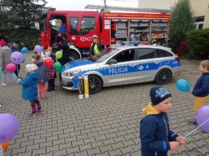 radiowóz stoi koło wozu strażackiego wokół których biegają dzieci