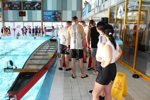 uczestnicy zawodów stoją przy łodzi umieszczonej w basenie