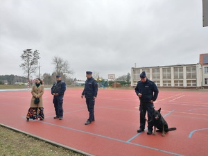 policjanci z psem i kobieta stoja na boisku szkolnym