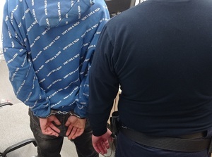policjant stoi z zatrzymanym, który ma założone kajdanki na ręce trzymane z tyłu