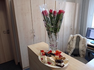 na stole stoi wazon z czerwonymi różami i talerz z ciastem